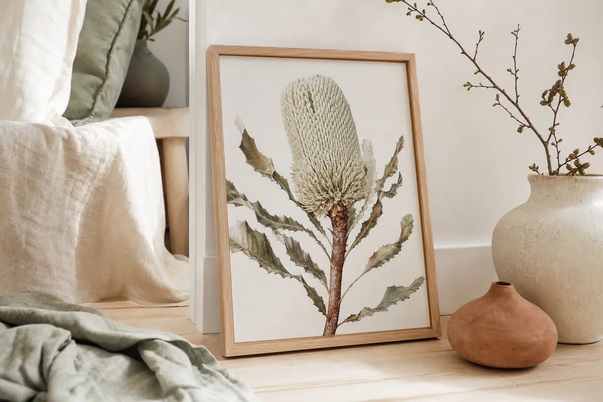 Framed banksia print leaning on a timber floor against a white wall